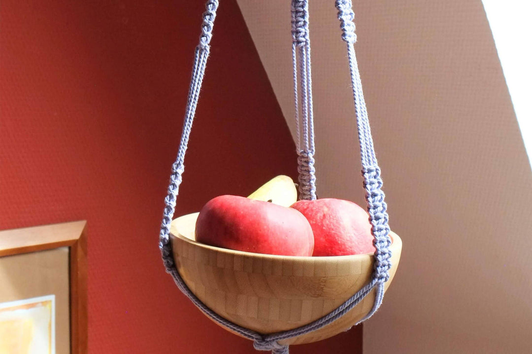 Ein hängender Obstkorb mit Makrameehalterung aus violettem Garn.